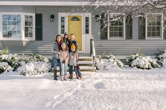 family of four in front of a home in the winter.