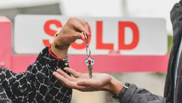 One hand giving key to another hand with sold sign.