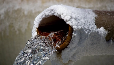 Snow-covered pipe with running water.
